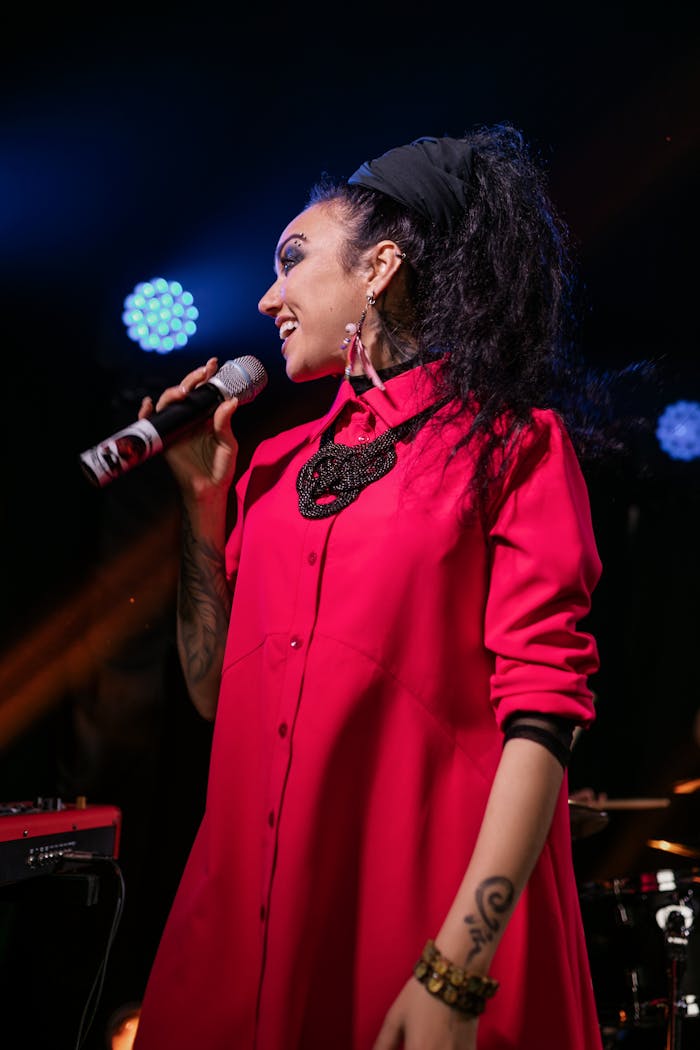 A vibrant female singer in a pink dress performing passionately at a concert.